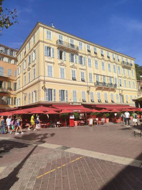 Güneşli bir sahil kasabasında kırmızı tenteli canlı bir kafe, canlı bir açık hava atmosferi yakalıyor.