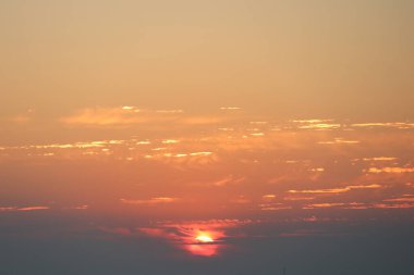 Alacakaranlıkta dalgalanan bulutların yanında canlı ve çarpıcı renklerin yer aldığı büyüleyici bir günbatımı sahnesi.