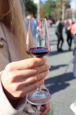 Zarif bir şekilde zarif bir el güzel bir şarap kadehini tutarken canlı, hareketli bir açık hava sosyal sahnesini yansıtır.