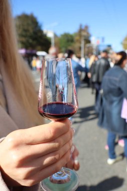 Zarif bir el, canlı ve canlı bir arka planda duran kırmızı şarapla dolu bir bardağı zarif bir şekilde tutuyor.