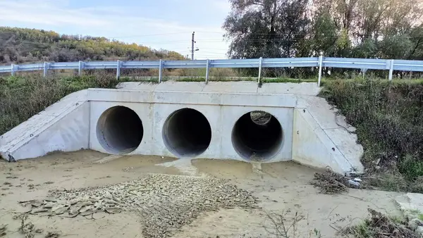 Üç büyük beton drenaj borusu bir yolun altından geçiyor. Resmedilmeye değer doğal bir manzaranın ortasına kurulmuş.