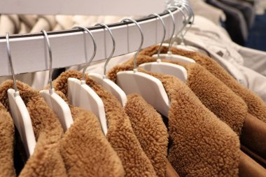 Modern bir giyim mağazasındaki askılarda düzgünce yerleştirilmiş birkaç şık kahverengi yün ceketin yakın plan görüntüsü.