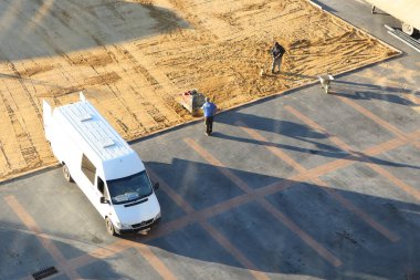 Birkaç işçi, inşaat alanında park halindeki bir minibüsün bitişiğindeki inşaat hazırlama faaliyetleriyle aktif olarak meşgul.