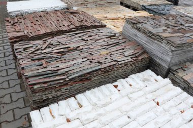 Kentsel bir alanda düzgünce sergilenen çeşitli inşaat malzemeleri, dokuları ve renkleri gösteren.