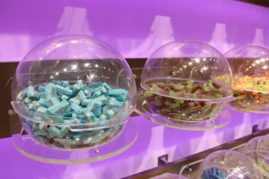 Modern bir rafta şeffaf kaplarda renkli bir tatlı çeşidi sergilenir.