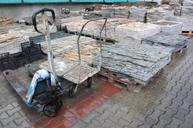 Bir inşaat sahasında istiflenmiş levhalar ve ulaşım için hazırlanmış bir palet kamyonu etkin bir şekilde sergileniyor.