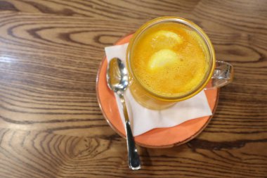 Temiz bir bardakta sıcak bir içecek, altın rengi sergiliyor, düşünceli bir şekilde ahşap bir masaya konuyor.