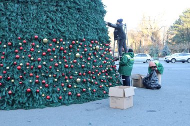 İşçiler neşeli bir atmosferde büyük bir Noel ağacına güzel ve şenlikli süslemeler yerleştiriyorlar.