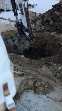 Büyük bir kazıcı kovası toprağın derinliklerine doğru kazıyor, yoğun bir inşaat alanında toprak ve enkazı ortaya çıkarıyor.