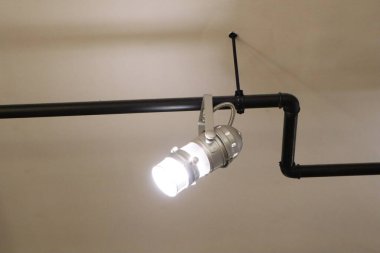 Bu parlak, modern ışıklandırma tasarımı endüstriyel borulara zarif bir şekilde monte edilmiş şık bir spot ışığı içeriyor.