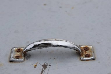 Yıpranmış bir yüzeyde paslanmış bir krom kabzanın yakın çekim görüntüsü, yaşını, aşınmasını ve yırtılmasını vurguluyor.