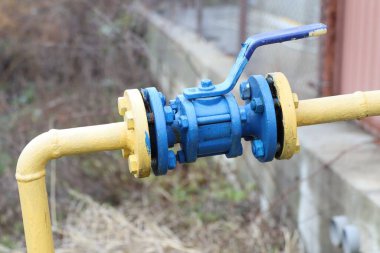 Endüstriyel ortamda sarı boruya bağlı mavi bir kapakçık içeren bir su sayacının detaylı bir yakın çekimi.