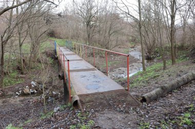 Yıpranmış bir yaya köprüsü, doğal çevrenin huzurlu ve huzurlu güzelliğinin tam ortasına yerleştirilmiş.