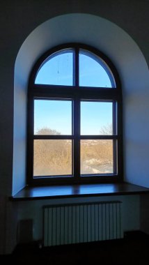 Huzurlu, kemerli bir pencere ardında huzurlu ve huzurlu bir manzarayı sergiliyor.