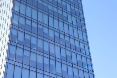 Modern cam ofis binası, berrak mavi gökyüzünü yansıtıyor, çağdaş mimariyi sergiliyor..