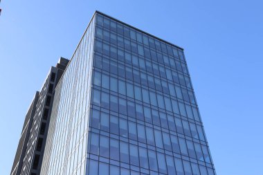 Çağdaş bir cam bina canlı mavi gökyüzüne karşı yükseliyor, modern şehir mimarisini gözler önüne seriyor.