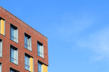 Köşe perspektifi, canlı bir gökyüzüne karşı geniş pencerelerle donatılmış çağdaş tuğla bir bina sergiliyor.