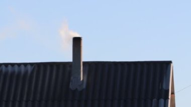 Bir baca, berrak mavi gökyüzünün arkaplanına, sıcaklığı ve rahatlığı somutlaştıran dumanlar salıyor.