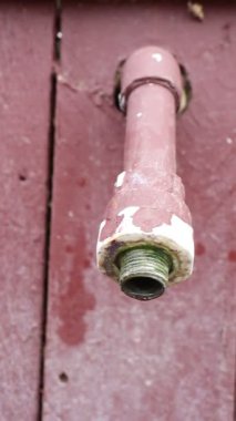 Eski, paslı bir boru yıpranmış ahşap bir duvardan belirgin bir şekilde dışarı çıkar, önemli bir aşınma ve yaşlanma belirtisi gösterir.