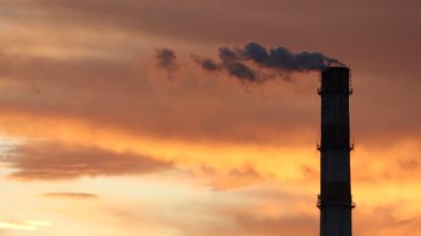 Nefes kesen gün batımına karşı yoğun duman yayan uzun bir bacanın çarpıcı görüntüsü.