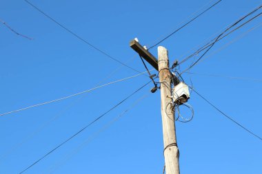 Kabloları olan sağlam bir ahşap elektrik direği canlı bir mavi gökyüzüne karşı yükseliyor ve kentsel altyapıyı gösteriyor.