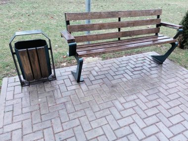 Asfaltlı yoldaki sağlam bir çöp tenekesinin yanında büyüleyici bir ahşap bank doğa ve rahatlama için mükemmeldir.