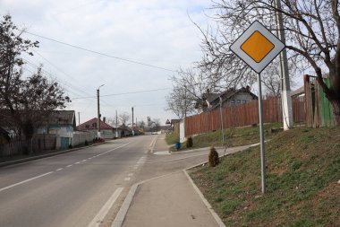 Bulutlu bir arka planda eşsiz ve kendine özgü bir trafik işaretinin yer aldığı sakin bir sokak sahnesi.