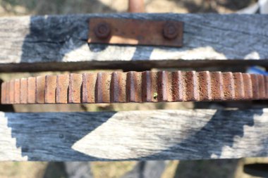 Ahşap bir yapıda paslı bir dişlinin yakın çekimi eşsiz dokusunu ve karmaşık çürümesini vurgular.