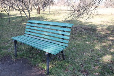 Bereketli ağaçların ve çevresini çevreleyen güzel doğal manzaraların arasına huzur içinde yerleştirilmiş sakin bir yeşil park bankı.