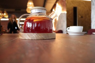 Ahşap bir masanın üzerinde, sıcaklığı ve rahatlığı çağrıştıran, zengin kırmızı çaydanlığın samimi bir tasviri.