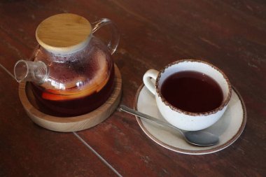 Nefis bir cam çaydanlık ve zarif bir bitkisel çay fincanı rahat bir sahnede, ahşap bir masada oturuyor.