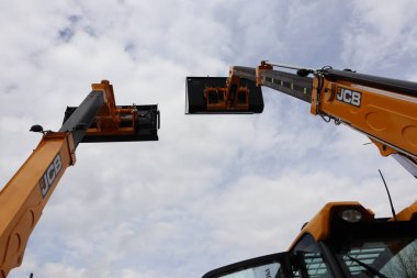 Kollarını gökyüzüne doğru uzatan iki JCB makinesinin çarpıcı görüntüsü inşaat gücünü gösteriyor..