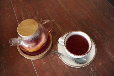 İşte güzel bir cam demlik ve ahşap bir masaya konmuş rahat bir fincan içeren büyüleyici bir çay seti.