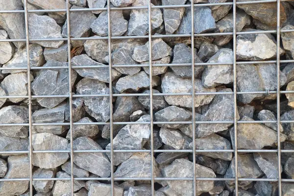 Bu yakın plan, peyzaj ve yapısal tasarım için kullanılan sağlam metalik bir ızgarada tutulan taşları gösteriyor.