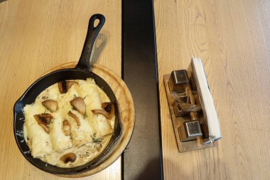 Ahşap bir masaya yerleştirilmiş kırsal bir tavada güzelce servis edilen lezzetli peynirli mantar yemeğinin tadını çıkar.