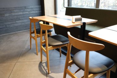 Şık bir kafeterya, gösterişli parlak ahşap masalar ve minimalist bir ortamda sandalyeler.