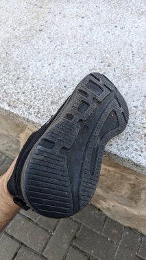Bu resim siyah bir spor ayakkabısının yakın çekimini gösteriyor, şehir ortamında eşsiz lastik izlerini vurguluyor