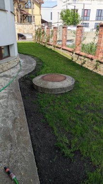 Güzel, bakımlı bir bahçe, yemyeşil, canlı otlar ve dekoratif bir rögar kapağı var.