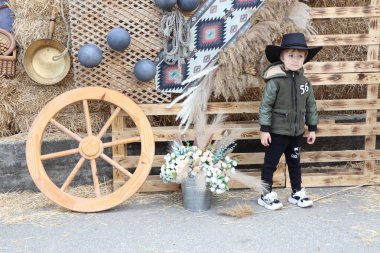 09.3.2025 Moldova Şık bir kovboy şapkasıyla süslenmiş genç bir çocuk büyüleyici kır süsleri ve canlı çiçekler arasında neşeli bir şekilde poz veriyor