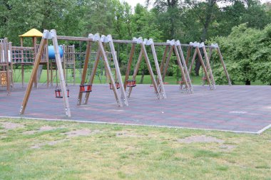 Canlı ve yemyeşil bir park geçmişine karşı çeşitli salıncakların yer aldığı sakin ve sessiz bir oyun alanı.