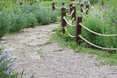 Yürüyüş boyunca canlı çiçeklerle süslenmiş, ahşap direkler ve iplerle kaplı sakin bir çakıl yolu.