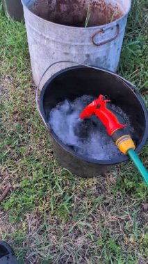 Uzun bir hortum siyah kovayı sabunlu suyla verimli bir şekilde doldurur ve açık hava sulama işlemini gösterir.