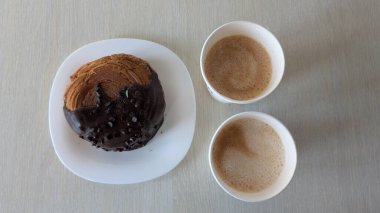 Lezzetli bir çikolatalı pasta, kırsal ahşap bir masada iki dumanı tüten kremalı kahvenin yanında servis edilir.