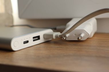 Taşınabilir bir güç bankası, ahşap bir yüzeyde bulunan bir USB kablosu kullanarak şu anda bir duvar şarj cihazına bağlanmış durumda.