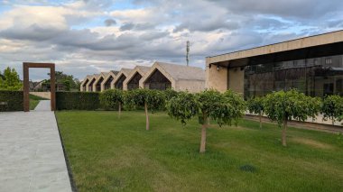 Modern mimari yapı yeşil ve çarpıcı bulutlar arasında duruyor, uyumlu bir denge yaratıyor.