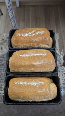 Üç mükemmel altın sarısı ekmek şimdi kendi pişirme tavalarında dinleniyor, dilimlenmeye hazır.