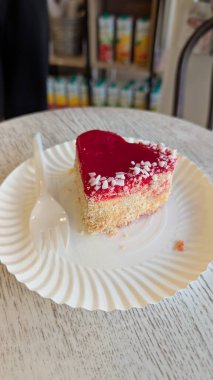 Kalp şeklinde pasta, kırmızı krema ve renkli şekerlerle süslenmiş. Doğum günleri ve düğünler için mükemmel.