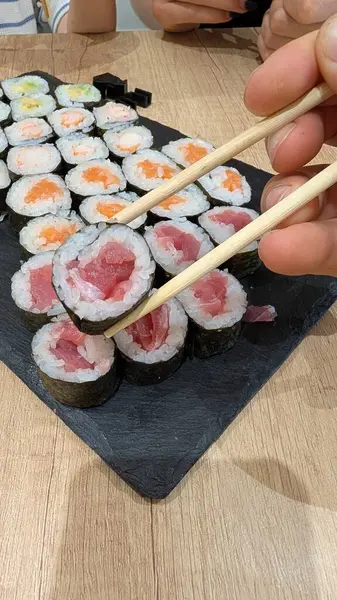 Yemek çubuklarının tuttuğu lezzetli suşi dürümlerinin yakın plan çekimi, canlı renklerini ve taze malzemelerini vurguluyor.