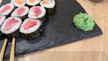 Taze suşi dürümleri, aromalı bir tahta üzerine güzelce ve düzgünce dizilmiştir. Yanında da aromalı bir parça wasabi.