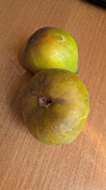 Mükemmel olgunlukta iki yeşil incir, güzel desenli ahşap bir masaya güzelce yerleştirilir, fotoğraf için hazır.